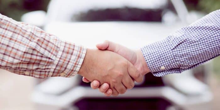 dealership salesman shaking hands with a customer after selling pre-owned cars.