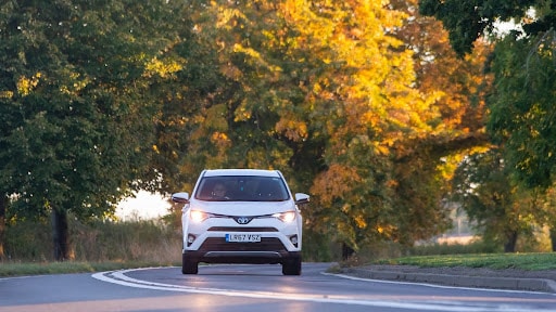 white hybrid electric Toyota Rav4 car on a country road in Autumn.