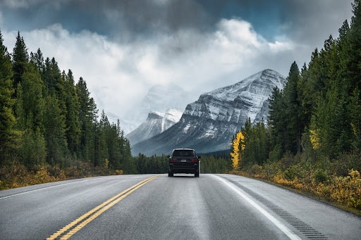 Rear view of a car driving on highway in the forest with mountain on gloomy at Banff national park.